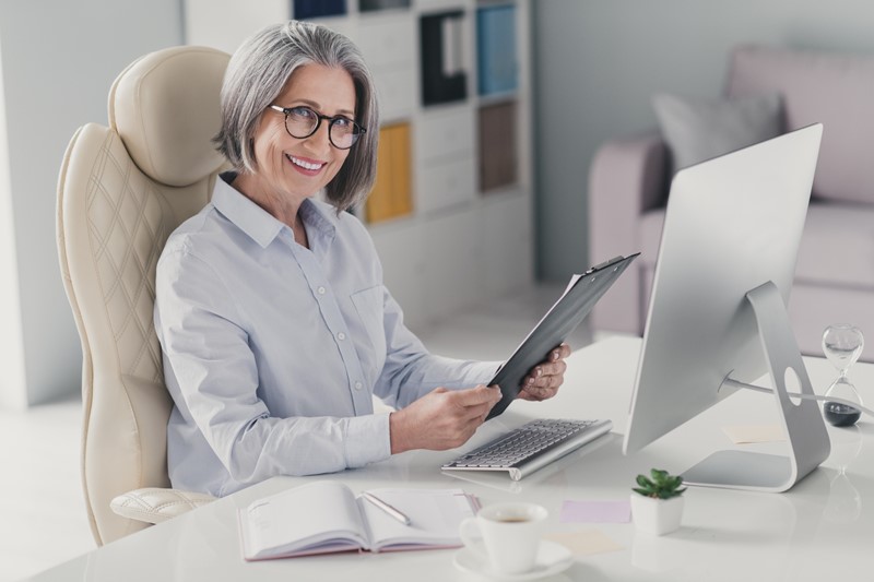 Oudere vrouw lachend achter haar bureau aan het werk