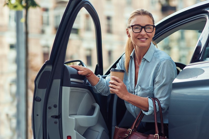 Lachende vrouw die uit de auto stapt met een koffiebeker to go