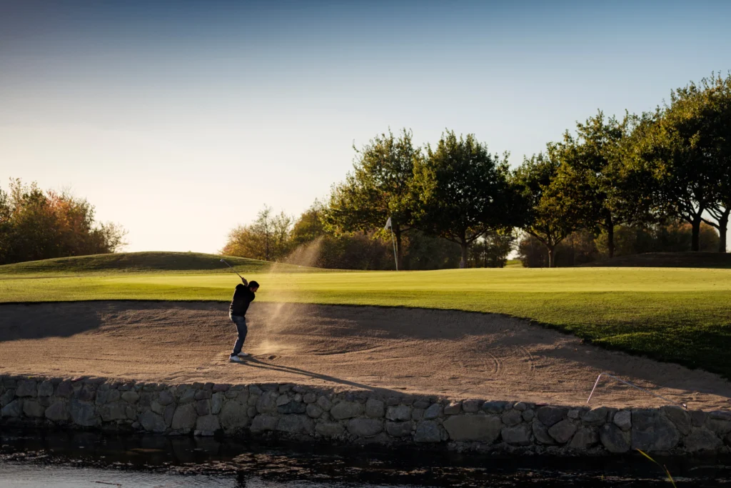 Golfer die vanuit een bunker de bal slaat richting de vlag en de green